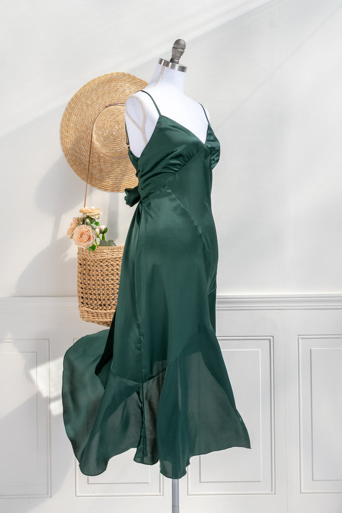 Beautiful wedding guest and formal dress in emerald green. French style feminine and romantic dress with straps, slit, and a bow. side view. Amantine dresses. 