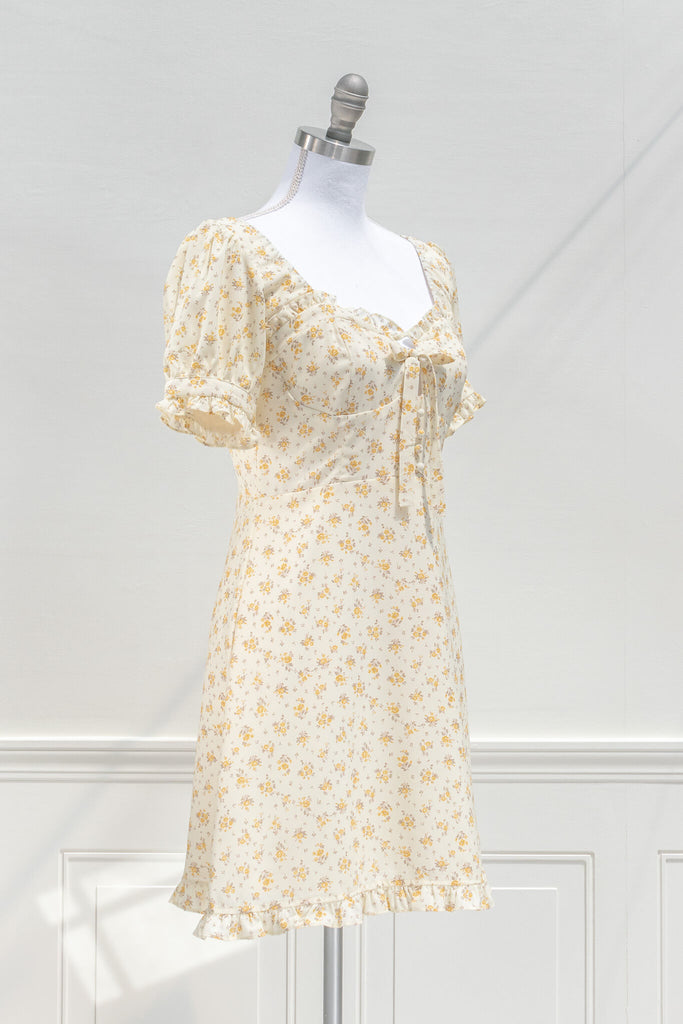 cottagecore dresses for spring - a mini yellow floral dress with a front bow, sweet heart neckline, and short sleeves. quarter side view. amantine. 